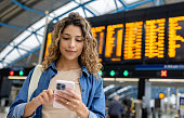 Woman at the train station using her phone while checking the departure board