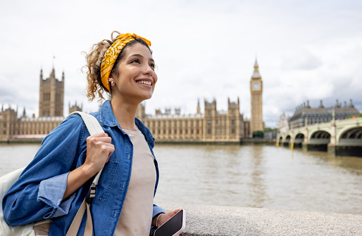 Happy Latin American woman sightseeing in London around the Big Ben and smiling
