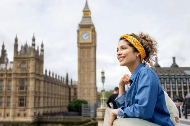 Happy female tourist in London looking at the view near the Big Ben while leaning against the bridge