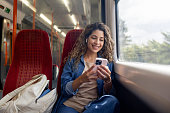Happy woman commuting on a train and checking her cell phone