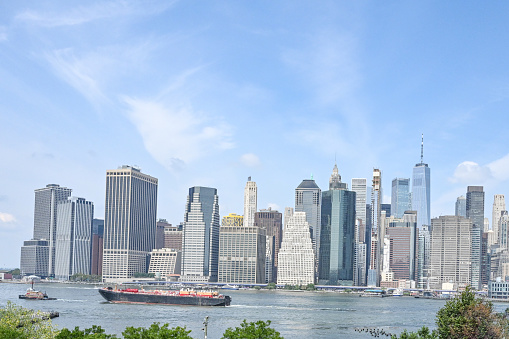 Skyline of Manhattan, New York. Downtown financial district on a clear sky day. Summer tree tops in the foreground. Large vessel is passing by along the skyline by the Hudson River. Beautiful summer day.