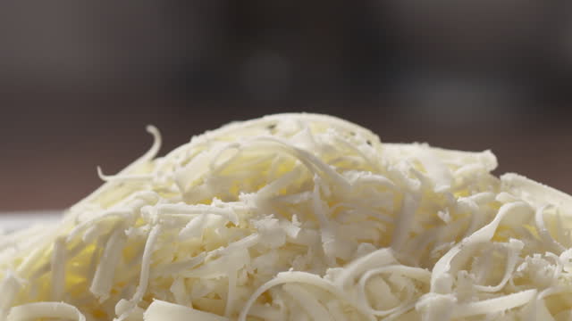 Slow motion slide back shot of grated pizza mozzarella cheese falls in plate