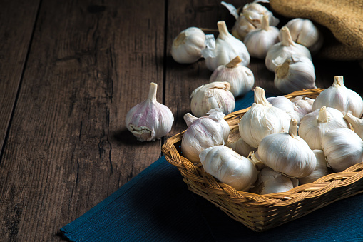 A lot of garlic is put in a basket placed on a wooden table.