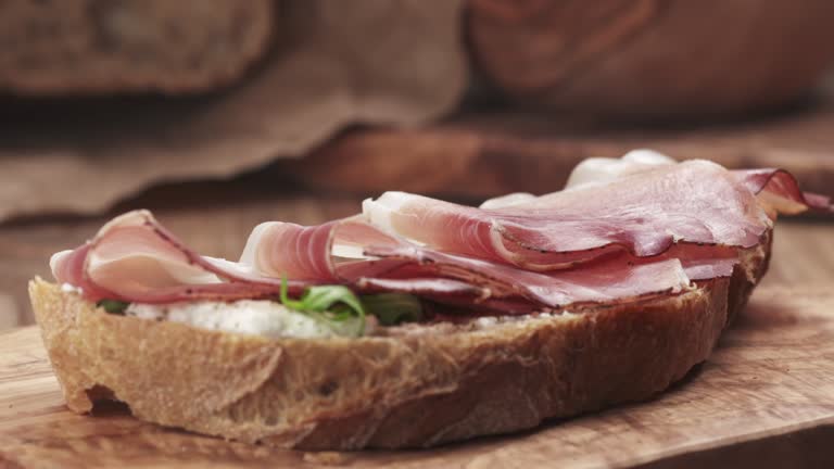 Slow motion of italian speck put on rustic bread with arugula and ricotta cheese