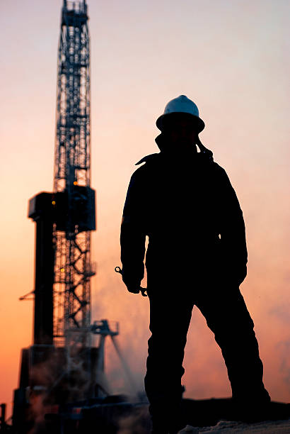 A petroleum worker is standing in front of the rig whith a wrench in his hand. aRGB.