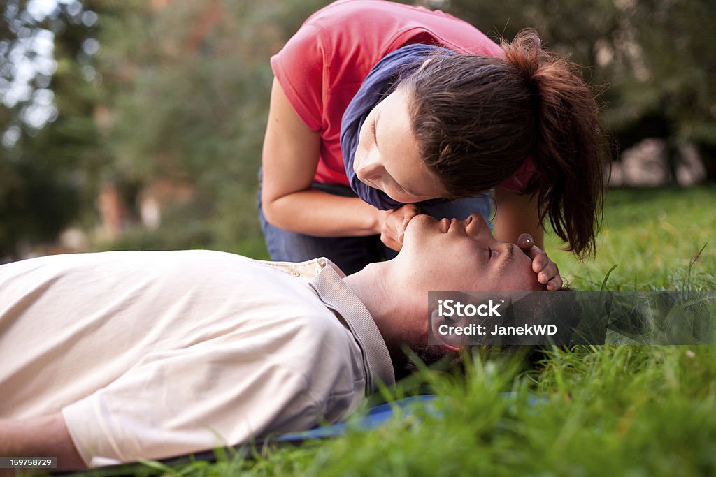 First aid - Look, listen and feel for breathing. First aid - Look, listen and feel for breathing. Woman is performing first and on a man laying in the grass. She is pulling his head back, listening to his breath and looking at his chest to check if he is breathing. The man is laying unconscious.  CPR Stock Photo