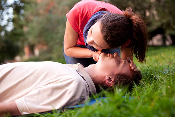 First aid - Look, listen and feel for breathing. First aid - Look, listen and feel for breathing. Woman is performing first and on a man laying in the grass. She is pulling his head back, listening to his breath and looking at his chest to check if he is breathing. The man is laying unconscious.  cpr stock pictures, royalty-free photos & images