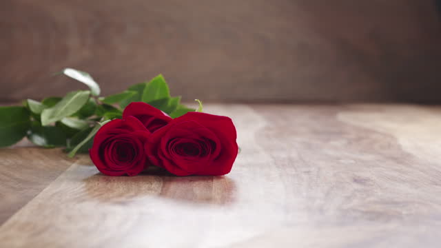 Slow motion of three red roses falling on old wooden table