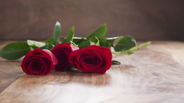 three red roses falling on old wood background in slow motion