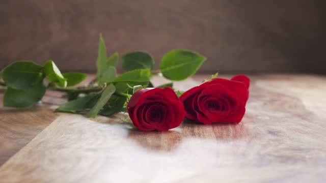 three red roses falling on old wood background in slow motion