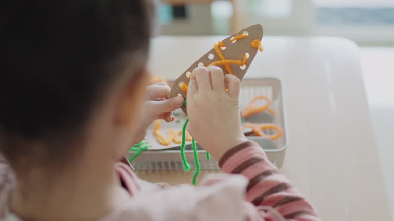 Preschool mixed girl threading a carrot shaped sewing card