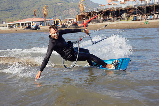 A young man kiteboarder scrapes the water with his hand inside