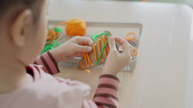 Preschool mixed girl threading a carrot shaped sewing card