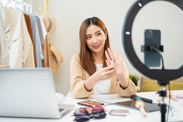 Young beautiful asian woman vlogger live broadcasting cosmetic makeup tutorial content with lipstick looking at cell phone. Influencers with various cosmetic recording review video sharing on social joven hermosa mujer asiática vlogger transmisión en vivo contenido tutorial de maquillaje cosmético con lápiz labial mirando el teléfono celular. los influencers con varias grabaciones cosméticas revisan el intercambio de videos en las redes sociales