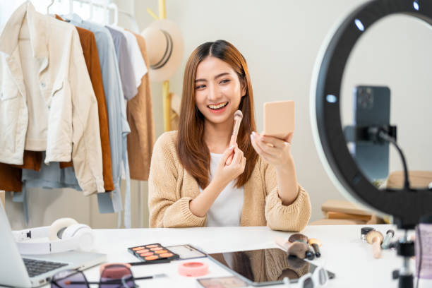 istock Young beautiful asian woman vlogger live broadcasting cosmetic makeup tutorial content with brush on looking at cell phone. Influencers with various cosmetic recording review video sharing on social 1597738727