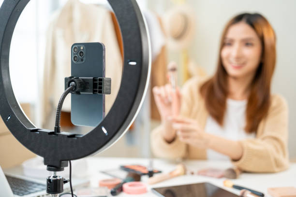 Young beautiful asian woman vlogger live broadcasting cosmetic makeup tutorial content with brush on looking at cell phone. Influencers with various cosmetic recording review video sharing on social joven hermosa mujer asiática vlogger transmisión en vivo contenido tutorial de maquillaje cosmético con pincel en mirar el teléfono celular. los influencers con varias grabaciones cosméticas revisan el intercambio de videos en las redes sociales