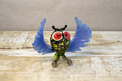 Bright glass owl figurine on rough wooden background front view