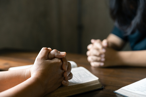 Group of family praying together, Christians and Bible study concept. Christian group of people holding hands praying worship to believe and Bible on a wooden table for devotional or prayer meeting.