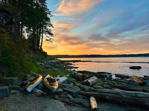Tribune bay sunset on Hornby Island on the Pacific Ocean in British Columbia in the Salish Sea. Beautiful colours with kayaks resting on shore amongst the driftwood while the sky dances with dramatic colours