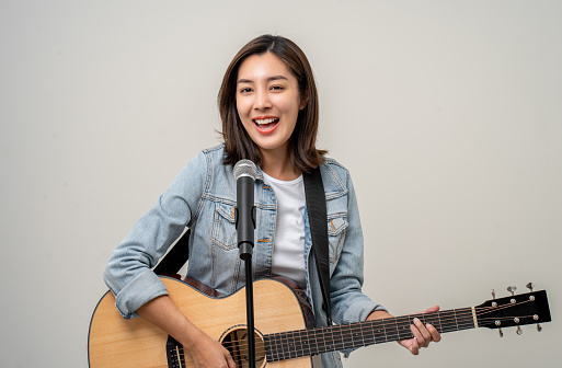 Happiness young asian woman singing song with guitar. Artist vocalist singer on isolated background. Confident woman public speaking talking with microphone in studio.