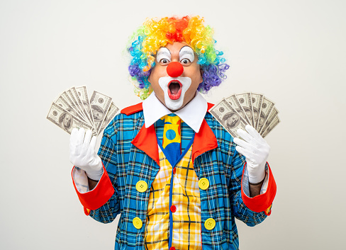 Mr Clown. Portrait of Funny face Clown man in colorful uniform standing holding a lot of money for gambling. Happy expression male bozo in various pose on isolated background.