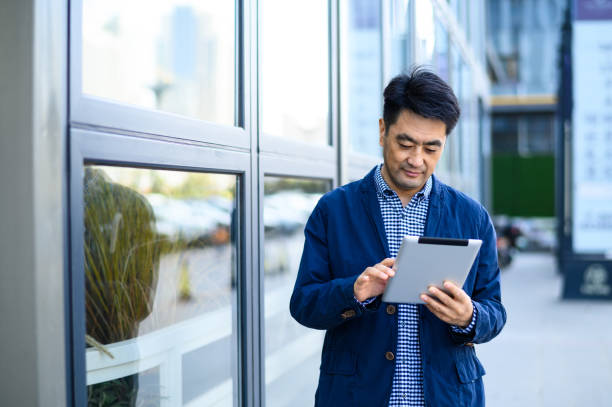 istock Asian middle-aged business man using digital tablet on city street 1597791421