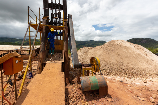 Mozambique - March 16, 2022: Miner feeding industrial ore crushing machine in industrial gold mineral extraction process