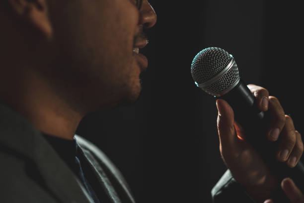 istock Confident successful speaker man talking on stage with spotlight strike through the darkness at corporate business event. Public speaker giving talk at conference hall. Stand up comedian. 1597809490
