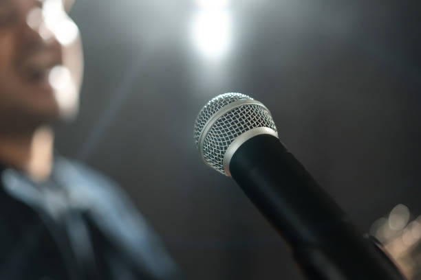 istock Attractive singer man singing music and playing guitar on stage with spotlight strike through the darkness at concert event. Musician performing live with light and smoke at hall. 1597810009
