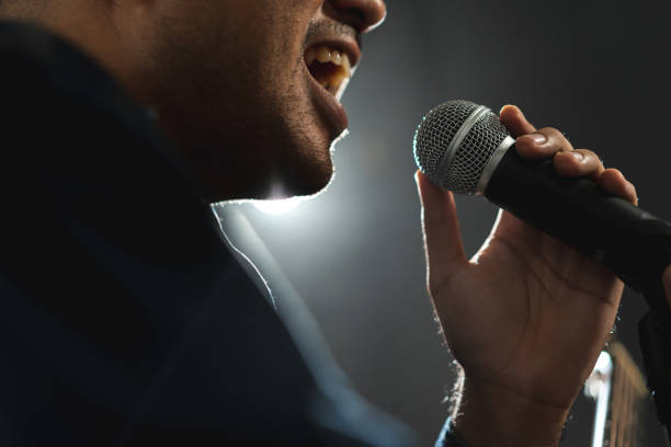 istock Attractive singer man singing music and playing guitar on stage with spotlight strike through the darkness at concert event. Musician performing live with light and smoke at hall. 1597810013
