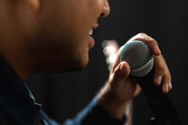 istock Attractive singer man singing music and playing guitar on stage with spotlight strike through the darkness at concert event. Musician performing live with light and smoke at hall. 1597810028