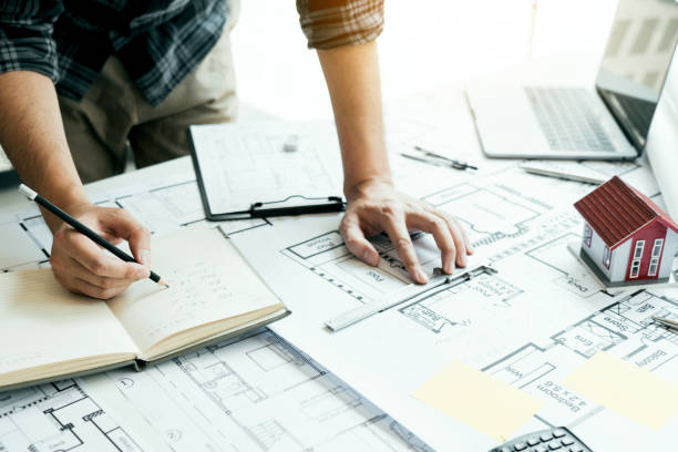 Interior designer or architect reviewing blueprints and holding pencil drawing on desk at home office. stock photo