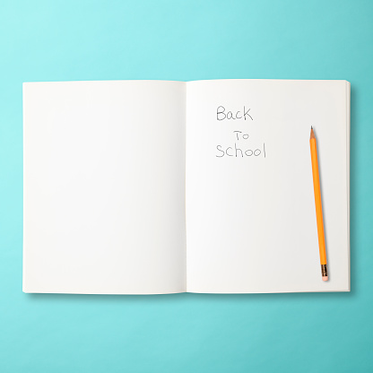 Words Back To School written on an open notebook with yellow pencil on light blue background.