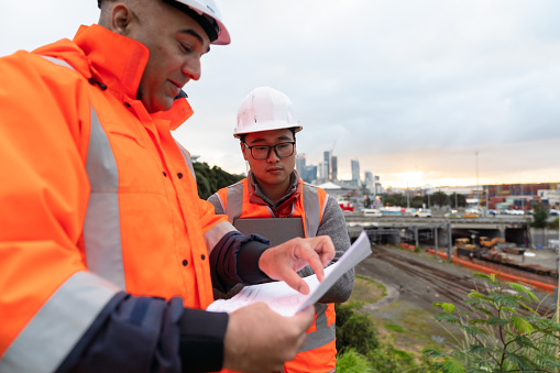 Two construction workers working using blueprints working standing at construction site.