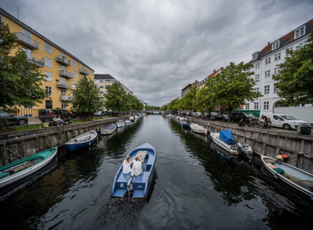 Copenhagen, Denmark - August 04, 2023: Christianshavn Canal surrounded by beautiful old apartment buildings, trees and boats, under an ominous cloudy summers sky.