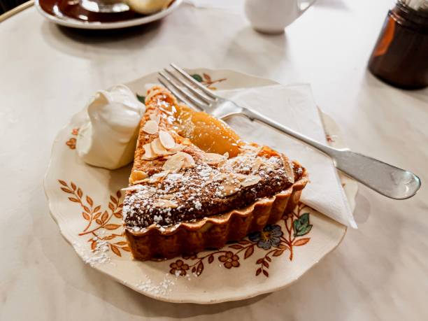 Horizontal high angle closeup photo of a slice of French style Pear and Almond Tart with whipped cream served on a vintage ceramic plate with a silver plate fork in a café restaurant. Mudgee, NSW.