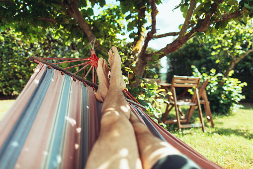 POV of summer relaxing and sunbathing on hammock: man feet while resting under a warm sun in Italy