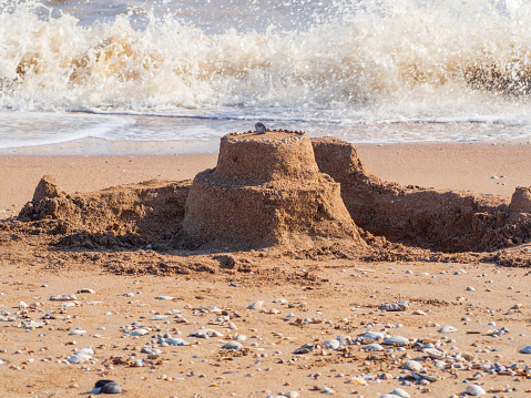 Sand castle on the beach with shells on the background of waves