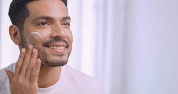istock Handsome young man applying cream at his face while standing in front of mirror in bathroom at home. 1598100699