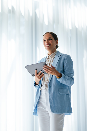 Low angle view of a smiling business woman using a digital tablet for a conference call while standing in her office.