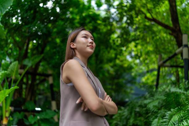 istock Business on the Move. Natural Balanced and Connected Mobility. Effortless Elegance. Young asian businesswoman carrying a laptop bag commuting to her work place in a central business district against the backdrop of lush green trees and gardens 1598107895