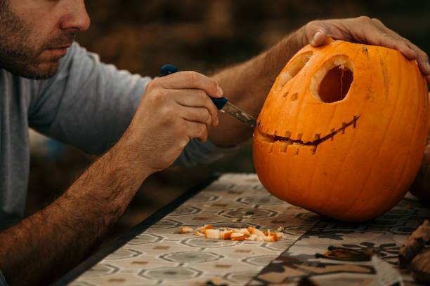 Getting ready for Halloween Man cutting and decorating a pumpkin for a Halloween. interconnect plug stock pictures, royalty-free photos & images
