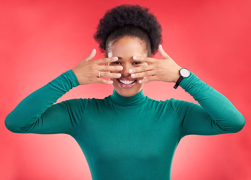 Hands, cover face and woman in studio with hiding and eyes peak with a smile. African female person, red background and happy with secret and model from Chicago with secret announcement and portrait