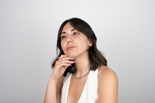 Portrait of a thougful woman looking up with sad facial expression over gray background. Horizontal. Studio shot.