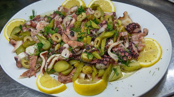 Boiled octopus salad is served with pure olive oil, lemon slices, dill, green olives and pickled cucumbers.  fresh and healthy seafood salad. Mediterranean gourmet appetizer.