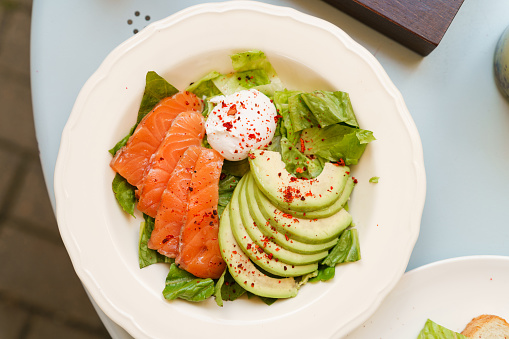 Plate with delicious and healthy morning breakfast. Poached egg, salmon slices, avocado and salad