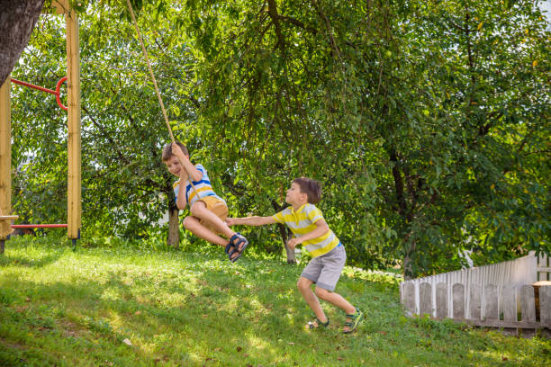 istock Two adorable happy little boys is having fun on a rope swing which he has found while having rest outside city. Active leisure time with children 1598151239