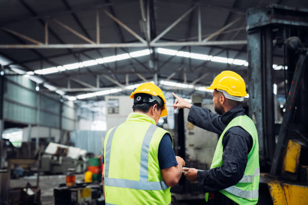 istock Industrious Engineer Operating Forklift in Warehouse. Efficient Forklift Driving in Factory. Engineer is working and maintaining in the factory. 1598153522