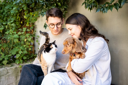 Young couple sitting in backyard holding a cat and a dog