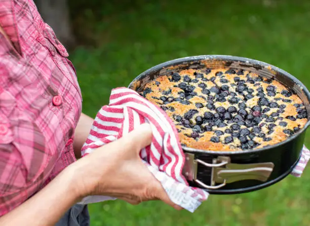 Woman holding a fresh baked cake or pie with blueberries in her hands outdoors in the garden. Closeup